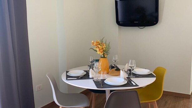 A dining area with a round table, four chairs, a flat-screen TV mounted on the wall, and a vase with flowers on the table. - Foria House Naples (Napoli)