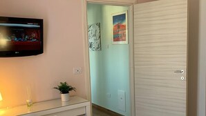 A hotel room with a bed, a desk with a chair, an air conditioner, a TV, and a door leading to another room. - Foria House Naples (Napoli)