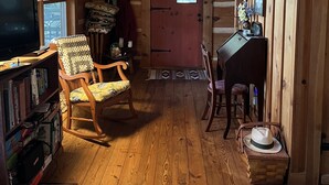 A cozy cabin interior with wooden walls, a television, a bookshelf, two rocking chairs, a desk, and a door with a window.
