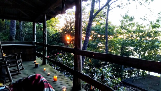 A wooden deck with a railing, surrounded by trees and a view of the forest.