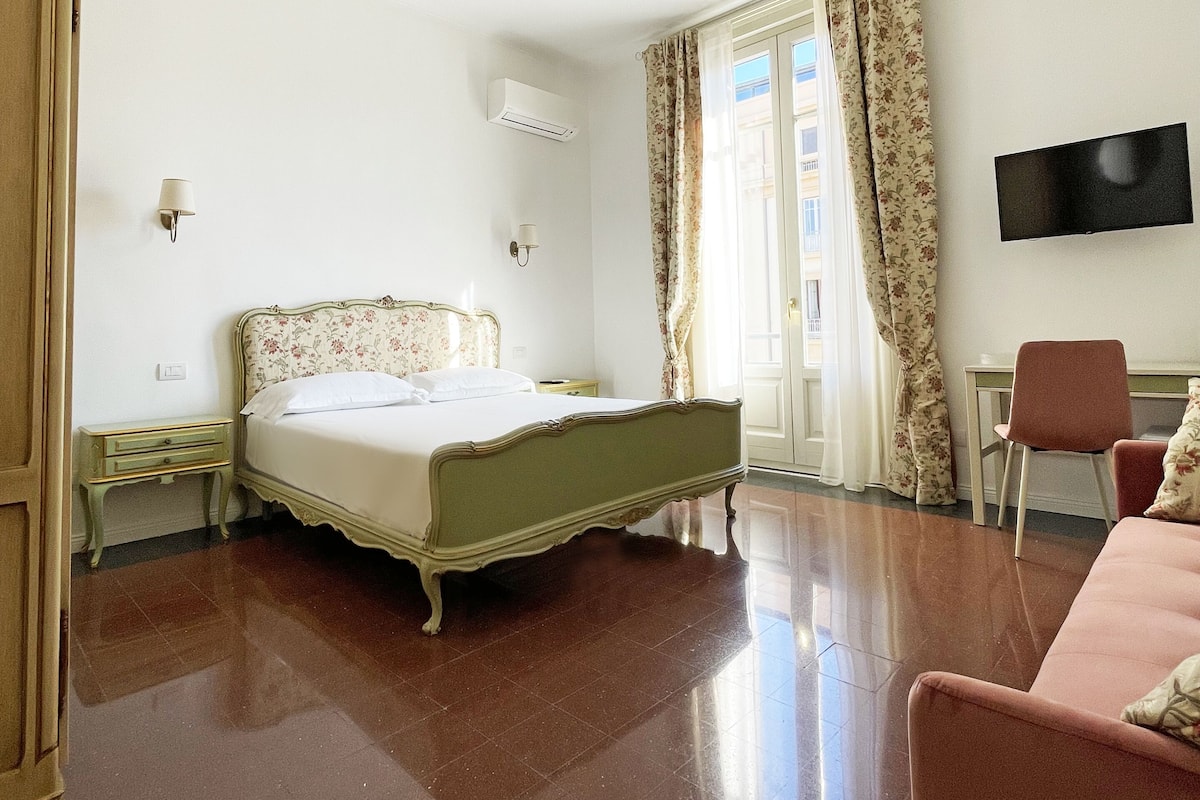 A bedroom with a bed, a desk, a chair, a TV, and an air conditioning unit.