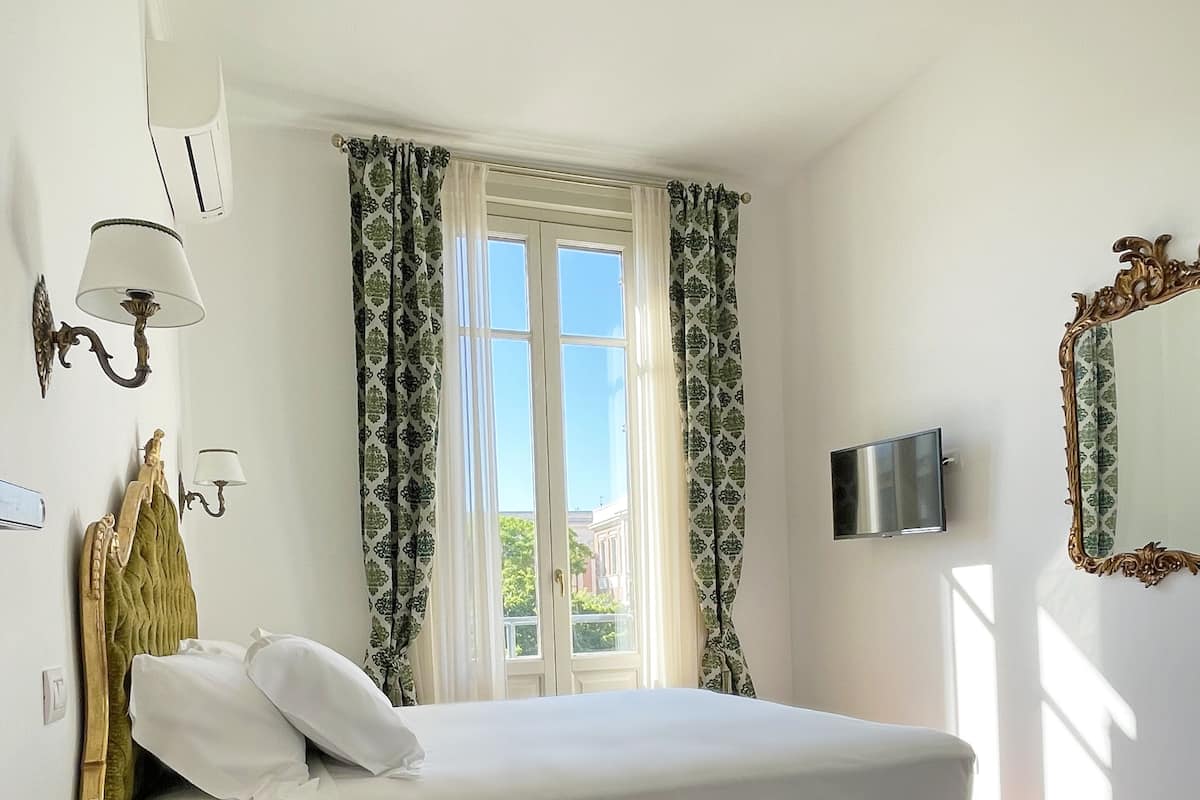 A bedroom with a bed, a television, a window with curtains, and a green decorative item.