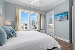 A bedroom with a large bed, a window with curtains, a TV on the wall, and a view of buildings outside.