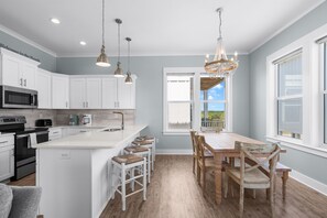 A modern kitchen with white cabinets, a central island, bar stools, and a dining table with chairs.