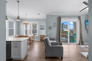 A spacious living area with a kitchen, dining table, and a view of a pool and buildings.