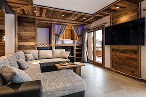 A modern living room with a sectional sofa, a flat-screen TV mounted on the wall, and wooden paneling on the walls and ceiling.