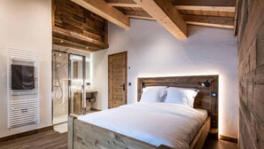Ein Schlafzimmer mit einem Holz-Kopfteil, einem Bett mit weißer Bettwäsche, einer Glasdusche und Holzboden.