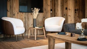 En moderne stue med to hvide lænestole, et træbord, et lille sofabord med en vase, og en grå sofa med et pelskast.