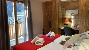 Quarto de hotel com cama, escrivaninha, cadeira, janela com cortinas e parede de madeira.