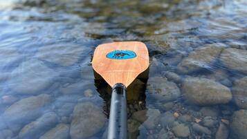 Gros plan d’une pagaie en bois ornée d’un logo, flottant sur une eau claire où l’on peut voir des petits galets.