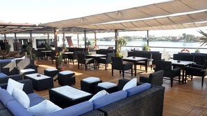 An outdoor seating area with tables and chairs, overlooking a body of water.