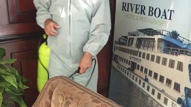 A person in protective gear standing next to a River Boat Hotel & Restaurants sign. - River Nile Boat (Cairo)