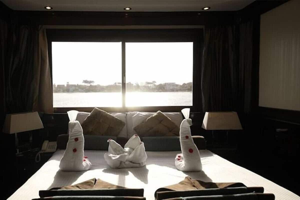 A room with a large window overlooking a body of water, a sofa with cushions, a table with a folded cloth, and two lamps.