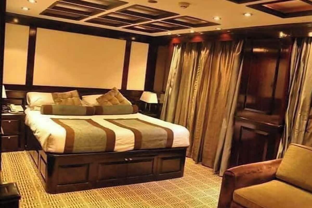 A hotel room with a large bed, a wooden headboard, a desk with a lamp, and a chair.