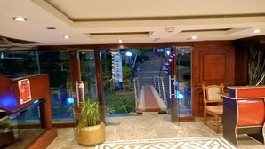A hotel lobby with a glass entrance, a reception desk, a staircase leading outside, and a potted plant.