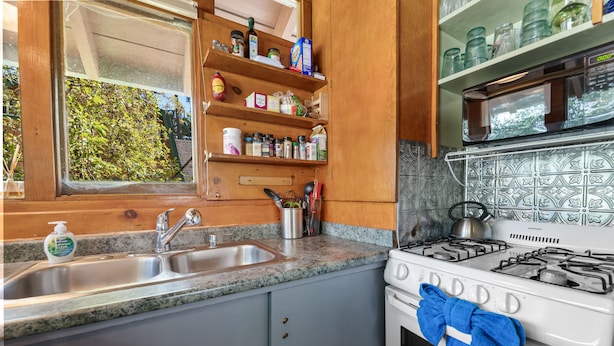 A kitchen with a granite countertop, stainless steel sink, wooden cabinets, and a white stove with a blue towel hanging on it. - Clerestory Cottage (Big Bear Lake)