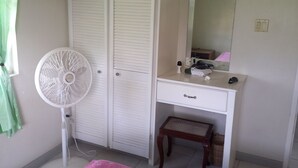 Un dormitorio con cama, escritorio, silla, ventilador y armario.