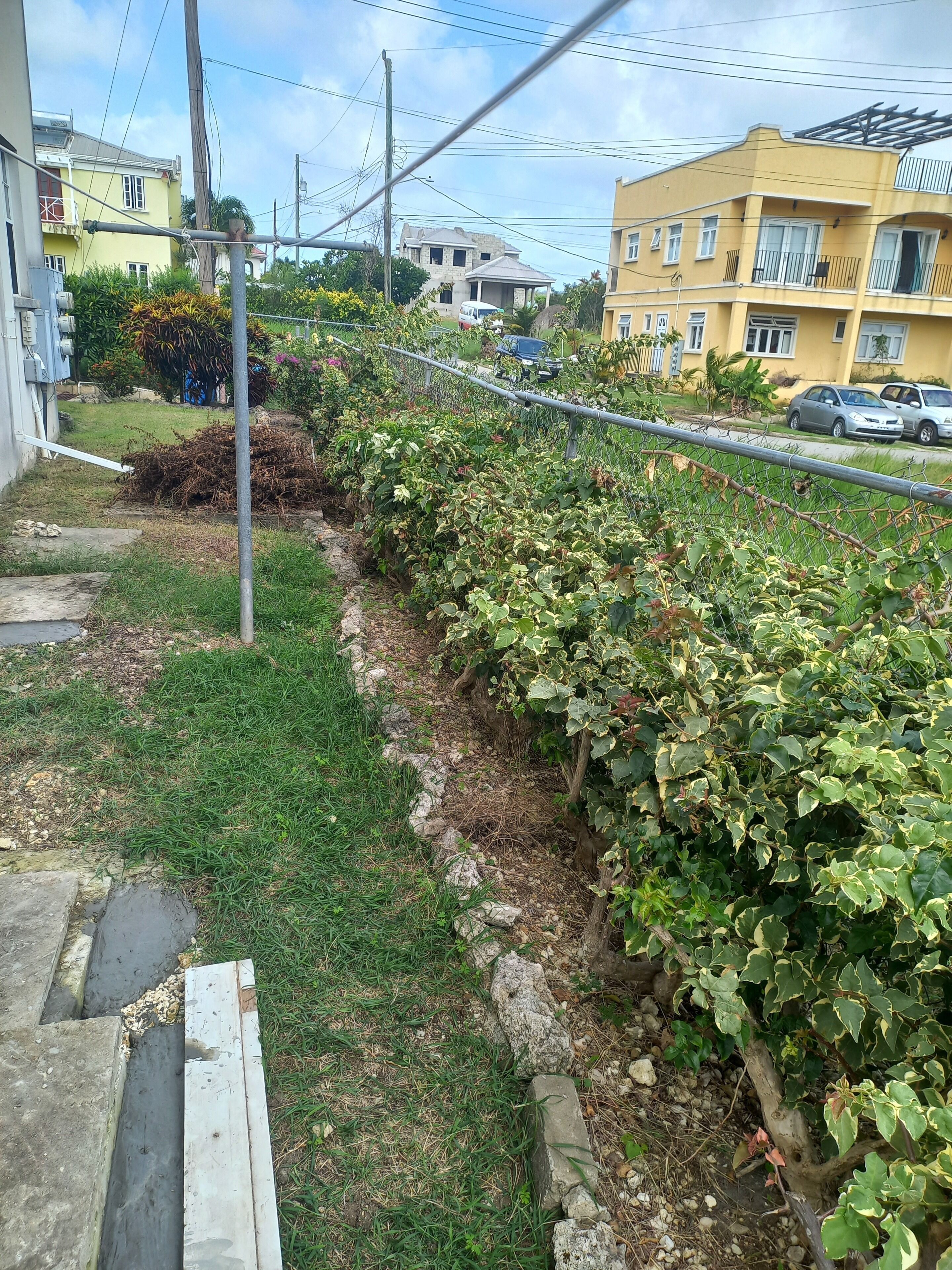 A residential area with a grassy yard, a fence, and a yellow building with balconies.