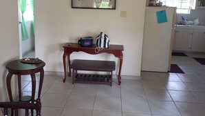 Una habitación con un banco de madera, una mesita, una obra de arte enmarcada en la pared y suelo de baldosas.