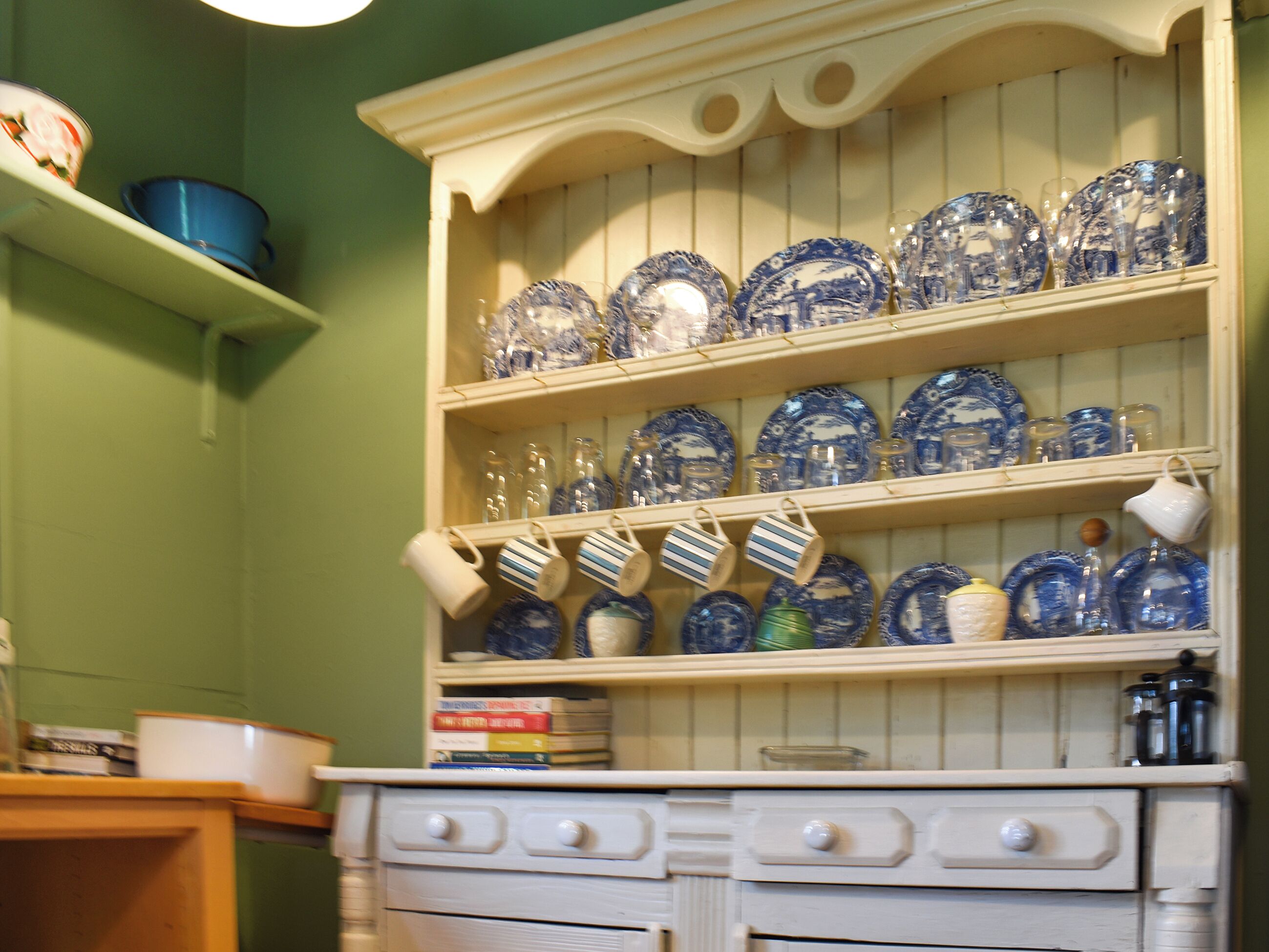 Une cuisine avec des meubles blancs, de la vaisselle en céramique bleue et blanche, et une étagère en bois.