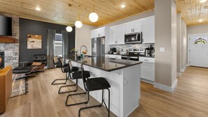 A modern kitchen with white cabinets, a large island, and a stone fireplace.