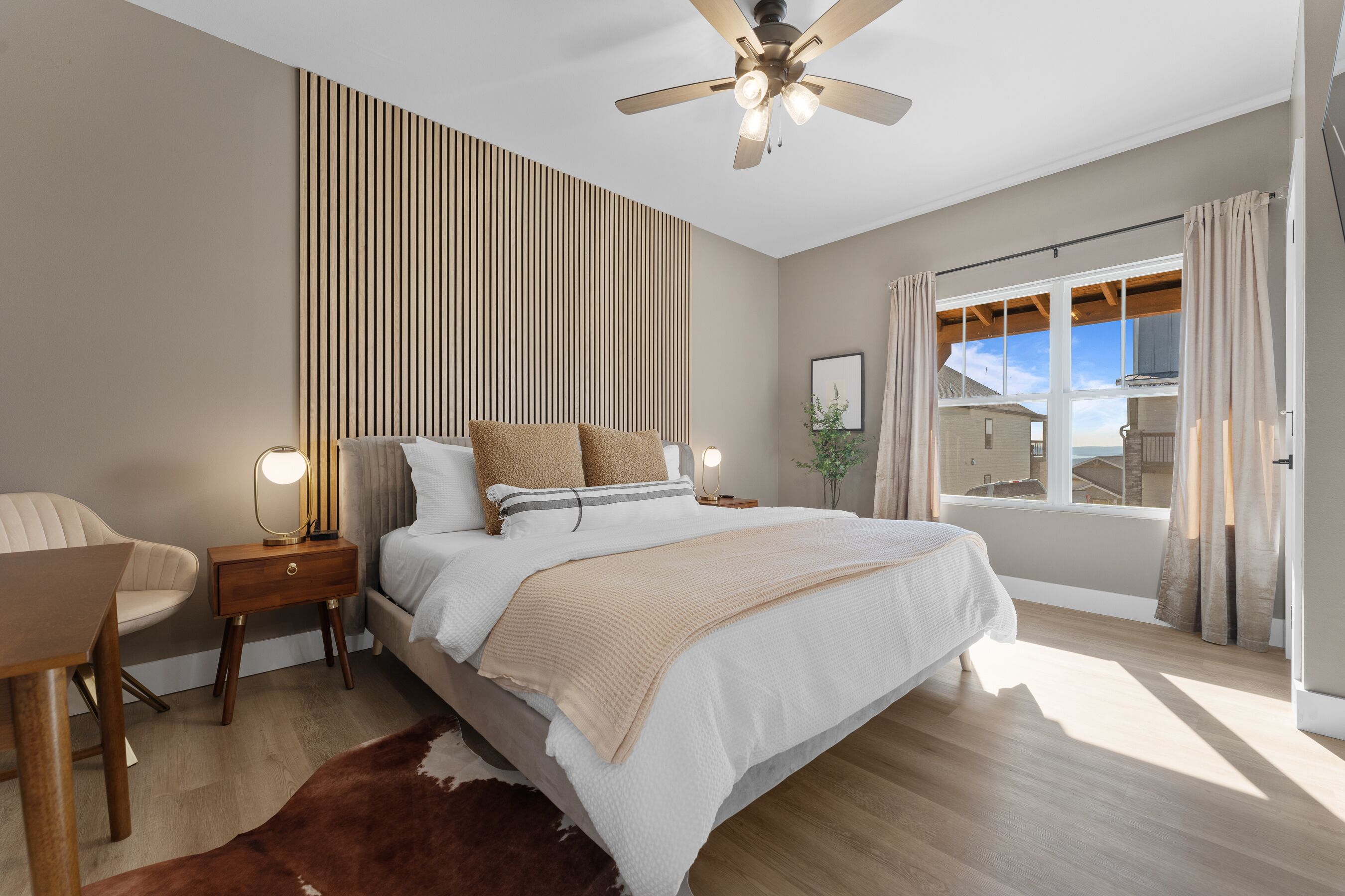 A modern bedroom with a large bed, bedside tables, a ceiling fan, and a view of the outside.