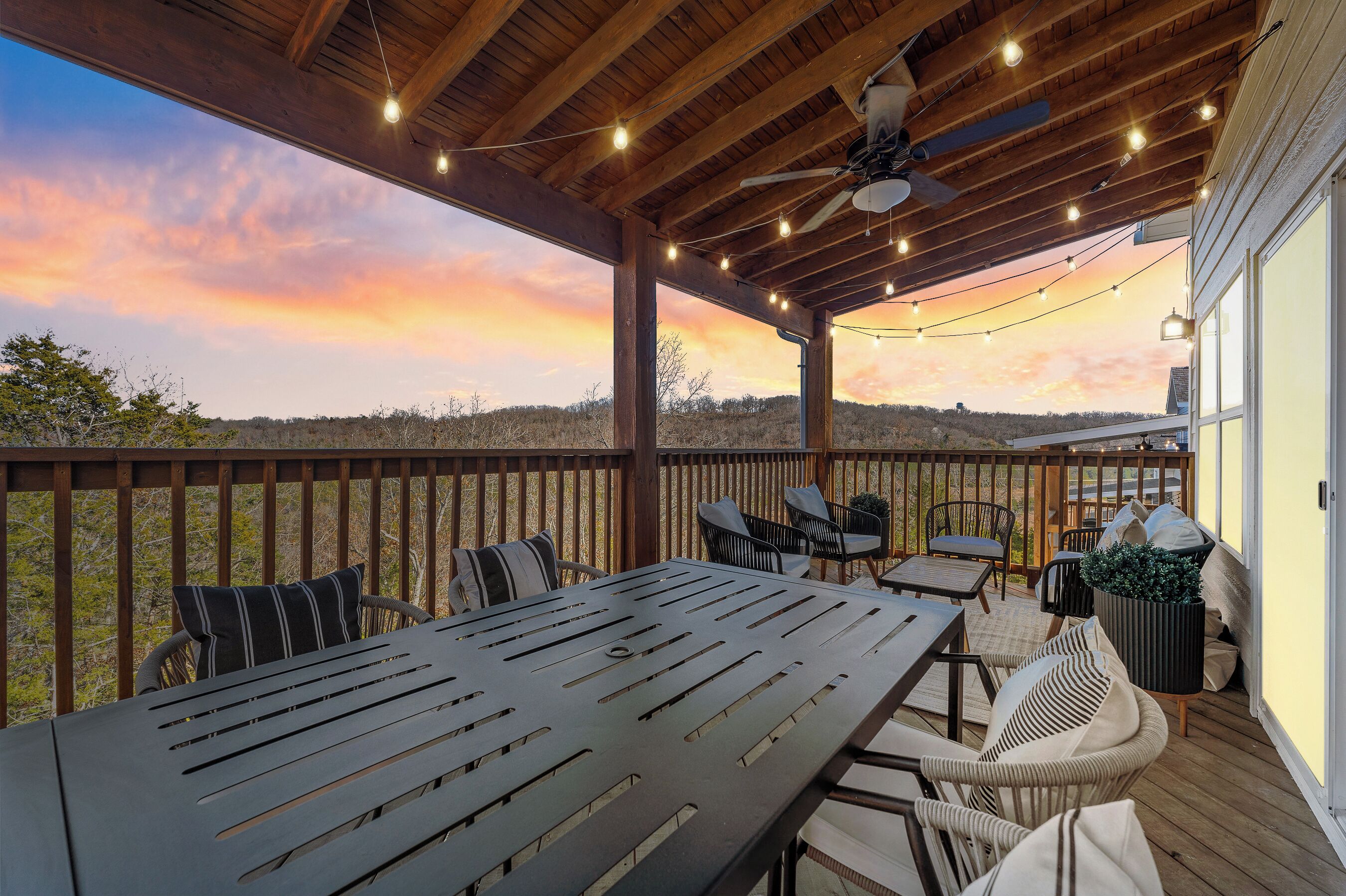 A covered outdoor deck with a table and chairs, a ceiling fan, and string lights.