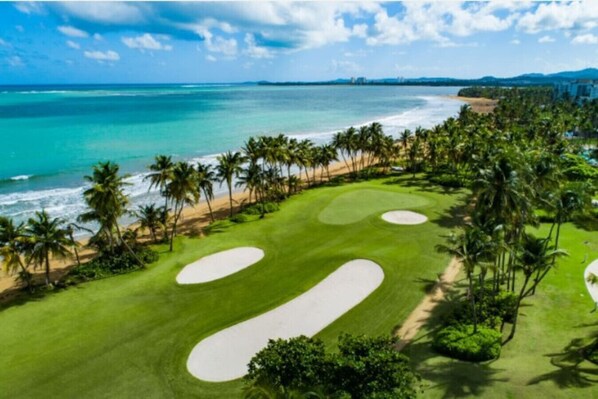 A golf course with sand bunkers and palm trees, overlooking a beach and ocean. - Beachfront Boutique Villa @ Wyndham Rio Mar Resort (Mameyes II)