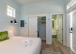 A hotel room with a bed, a green bicycle pillow, a towel rack, and a closet with hanging clothes. - Romantic, Cute Cottage on Anna Maria Island. Close To Everything. Pet Friendly! (Bradenton Beach)
