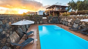 A swimming pool with lounge chairs and umbrellas, surrounded by stone walls and a wooden deck.