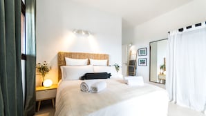 A modern hotel room with a large bed, a bedside table with a lamp, a mirror, and a view of the outdoors.