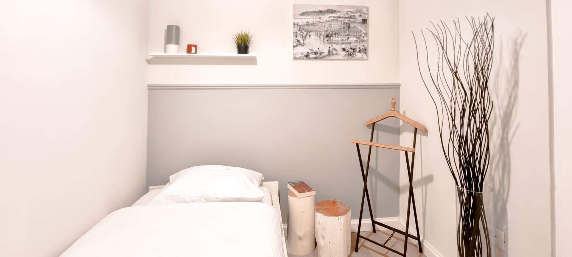 Un dormitorio con cama, una mesita de noche, un estante en la pared con una planta y un cuadro.