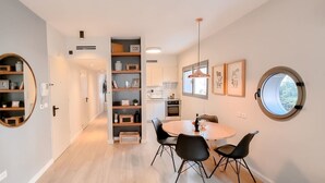 A modern kitchen with white cabinets, a round dining table with black chairs, and a large window providing natural light. - Ness Tsiyona Cachemire (Tel Aviv)