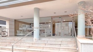 A modern building entrance with a staircase, glass doors, and a bicycle parked outside. - Ness Tsiyona Cachemire (Tel Aviv)