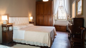 A bedroom with a large bed, wooden wardrobe, and a window with curtains. - Appartamento L'antico Rione (Piazza)