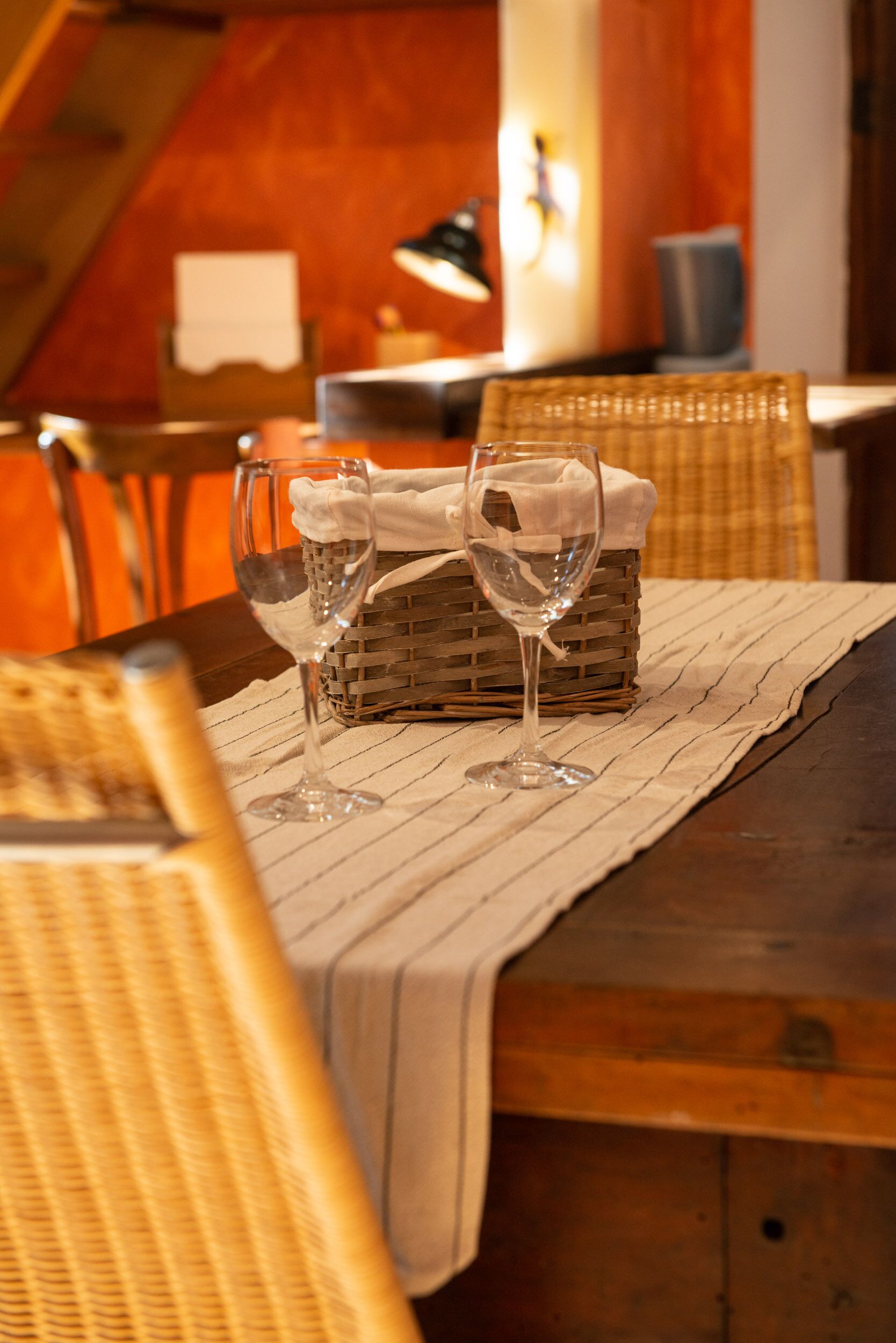 Una mesa de comedor con dos copas de vino y una cesta, sobre un mantel a rayas.