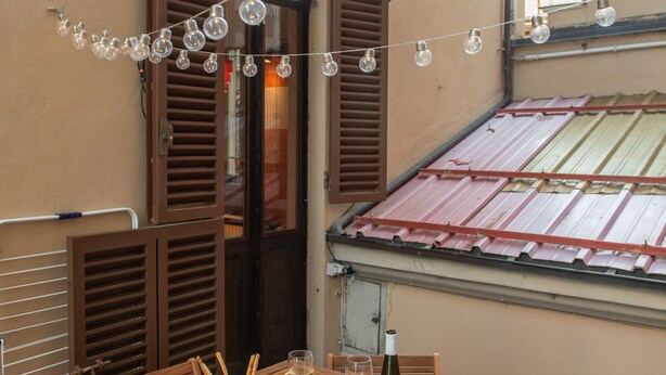 A wooden table with a bottle of wine and glasses, set against a beige wall with brown shutters. - Appartamento L'antico Rione (Piazza)