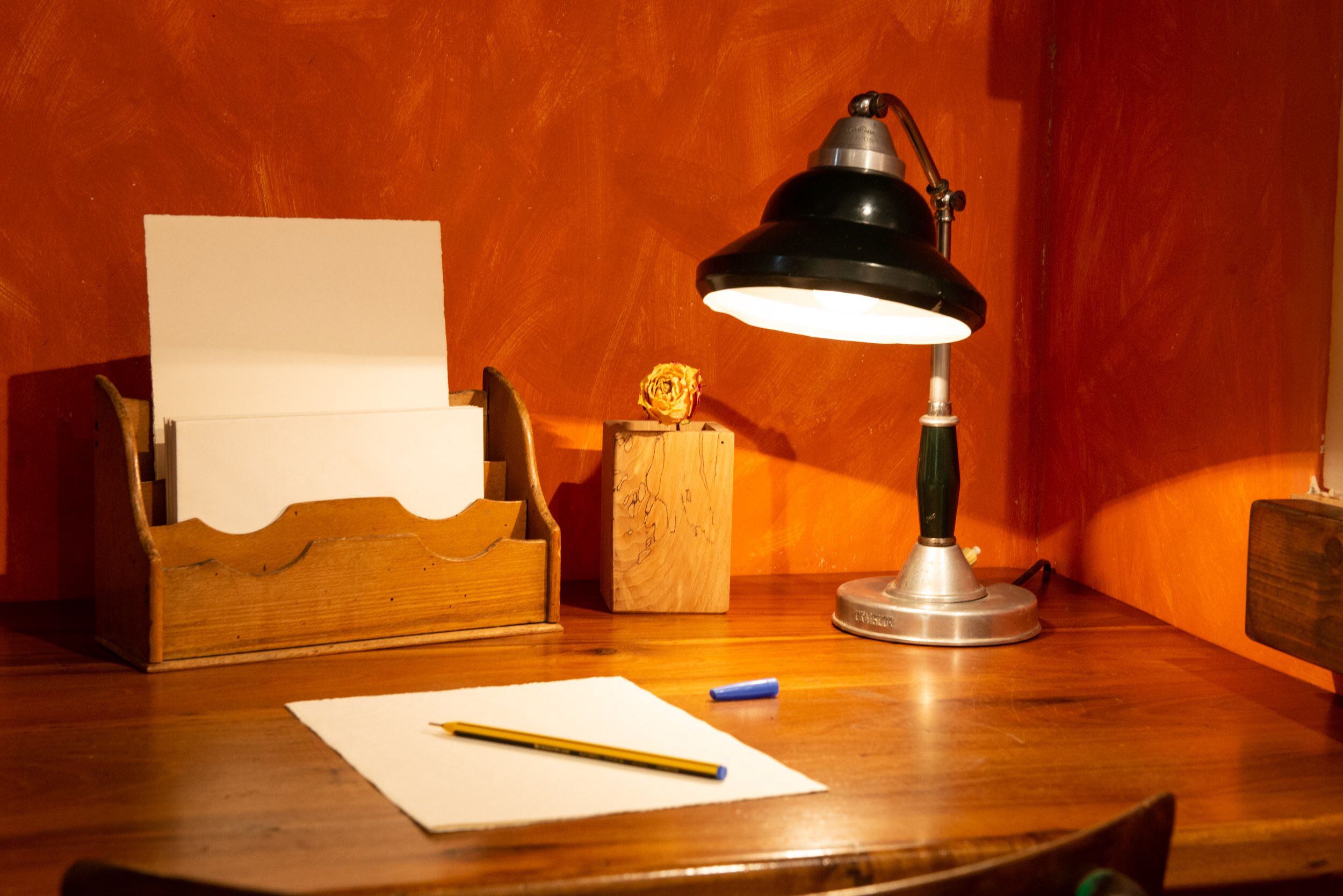 Un bureau en bois avec une lampe de bureau, un crayon, une feuille de papier et une petite boîte en bois contenant une fleur.