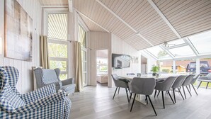 A spacious room with a dining area, a television, and a view of the outside. - Ferienhaus Ostseele mit Whirlpool, Dampf- und Normale Sauna Sowie Kamin (Brodersby)