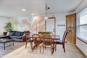 Uma área de refeições com uma mesa de madeira, cadeiras e um mural na parede.