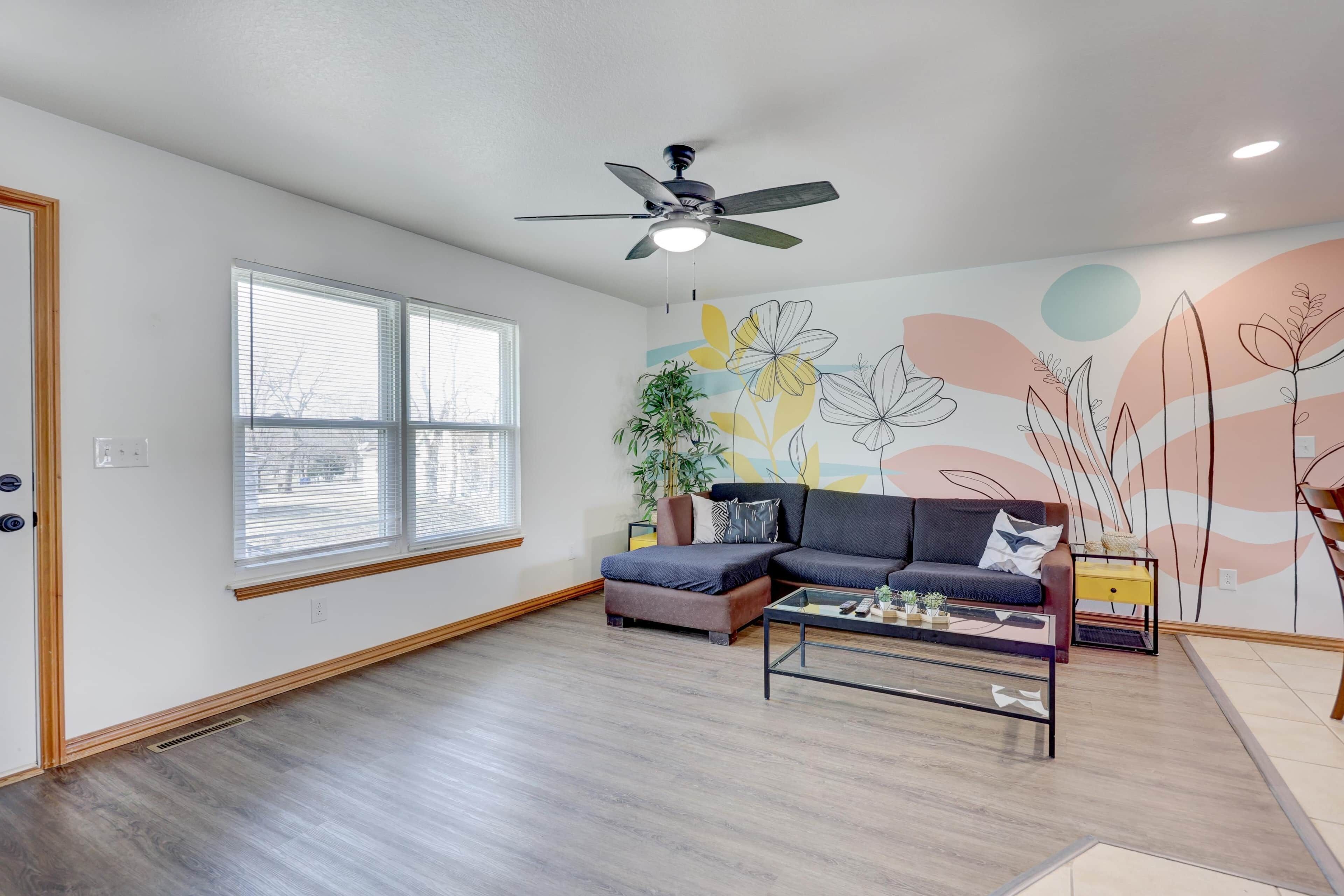 A modern living room with a sectional sofa, a coffee table, a ceiling fan, and a large window with blinds.