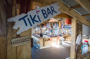 Un bar de madera rústica con un letrero que dice "TIKI BAR" y un rótulo con el lema debajo.