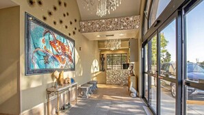 A lobby with a large abstract painting, a reception desk, and a view of the street through large windows. - The Colony - Oceanfront 2BR/2BA - Great Views! (Virginia Beach)