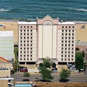 Et hotel med et centralt tårn og en mindre bygning på hver side, beliggende nær en strand med synlige bølger.