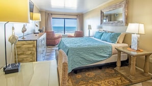 A hotel room with a bed, two chairs, a desk, a lamp, and a view of the ocean. - The Colony - Oceanfront 2BR/2BA - Great Views! (Virginia Beach)