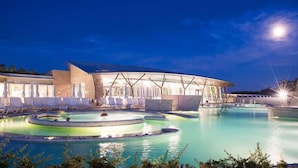 Resort com ampla área de piscina, espreguiçadeiras e um edifício peculiar com telhado curvo.