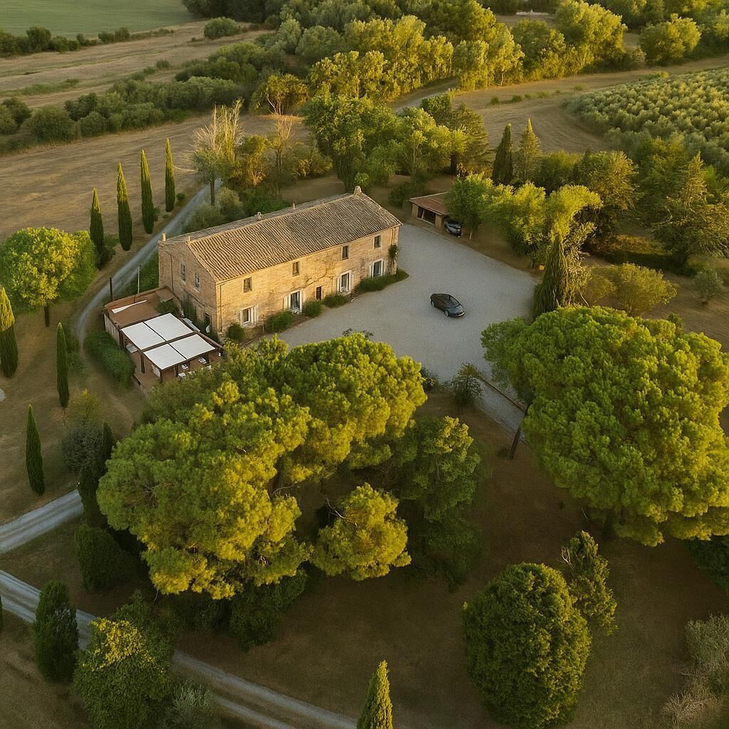 An aerial view of a stone house with a courtyard, surrounded by trees and fields.