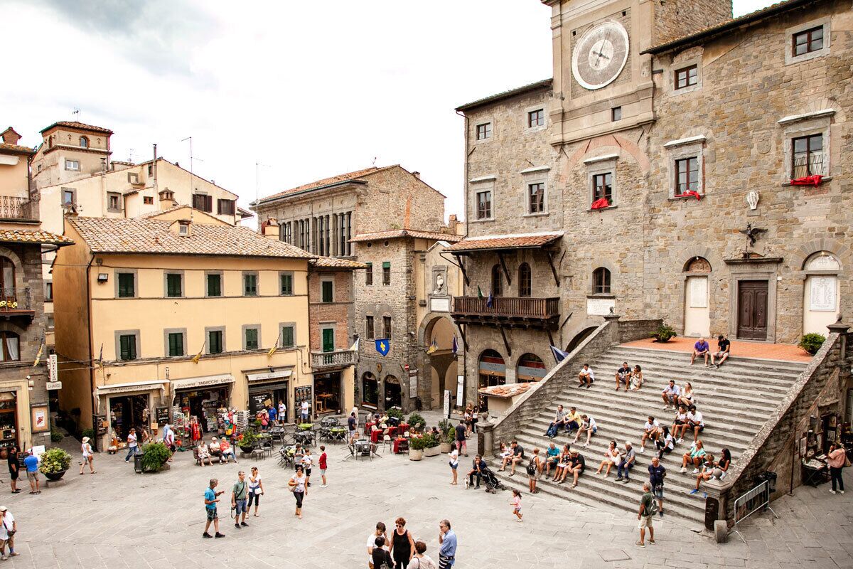 Una piazza vivace con edifici storici, una torre dell'orologio e una scala che conduce a un livello superiore.