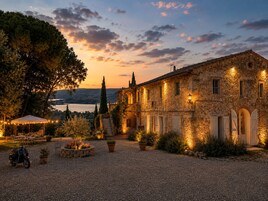 Un edificio de piedra con un patio de grava, mobiliario exterior y vista al agua.