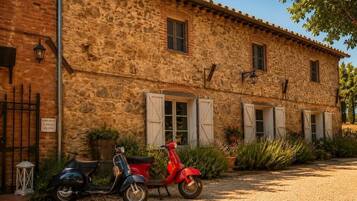 Un bâtiment en pierre à l’aspect rustique, avec une allée pavée et deux scooters garés devant.